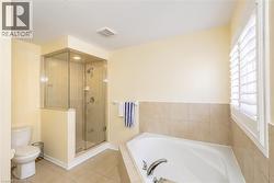 Bathroom featuring a corner soaking tub with tile surround, a glass-enclosed shower with tile walls, and a window with plantation shutters - 