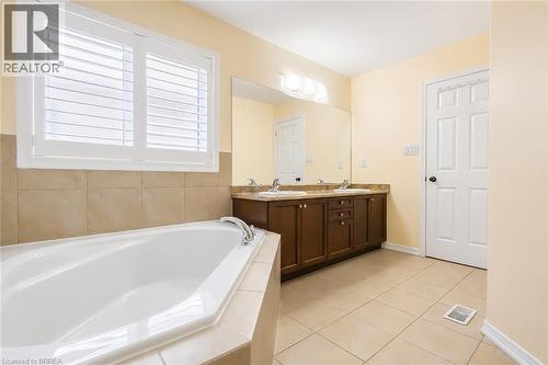 Bathroom featuring a built-in corner bathtub, plantation shutters, a dual sink vanity with brown cabinetry, a large mirror, and tile flooring - 26 Pollard Street, Brantford, ON - Indoor Photo Showing Bathroom