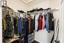 Walk-in closet featuring white perimeter shelving, multiple hanging rods, and wood-finish flooring - 