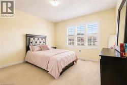 Carpeted room featuring a ceiling-mounted light fixture, light yellow walls, white baseboards, and a triple window with white plantation shutters - 