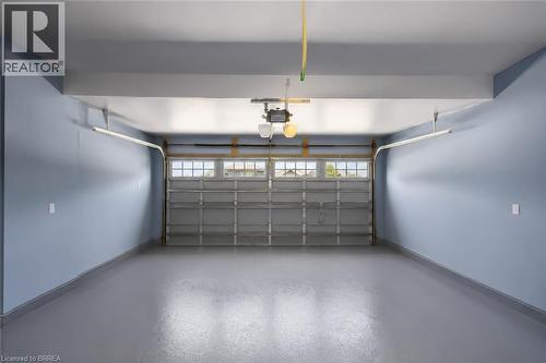 Spacious garage featuring a durable gray epoxy floor, light blue painted walls, an automatic garage door opener, and a garage door with upper window panels - 26 Pollard Street, Brantford, ON - Indoor Photo Showing Garage