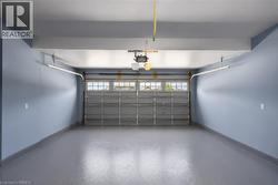 Spacious garage featuring a durable gray epoxy floor, light blue painted walls, an automatic garage door opener, and a garage door with upper window panels - 