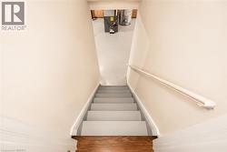 Stairwell with painted treads and risers, white handrail, light-toned wall paint, and wood-finish flooring at the base - 