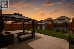 Expansive backyard featuring a concrete patio, a metal gazebo with string lighting, a wooden privacy fence, and a storage shed - 