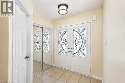 Double entry doors with intricate ironwork glass panels, tiled flooring, an overhead flush-mount light fixture, and mirrored closet doors - 26 Pollard Street, Brantford, ON - Indoor Photo Showing Other Room