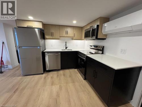 Kitchen featuring light wood-finish upper cabinetry, dark base cabinetry, light countertops, a stainless steel appliance suite, and wood-finish flooring - 431 Krug Street, Kitchener, ON - Indoor Photo Showing Kitchen