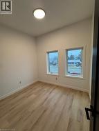 Room featuring wood-finish flooring, white walls, two windows, a ceiling-mounted light fixture, and white baseboards - 