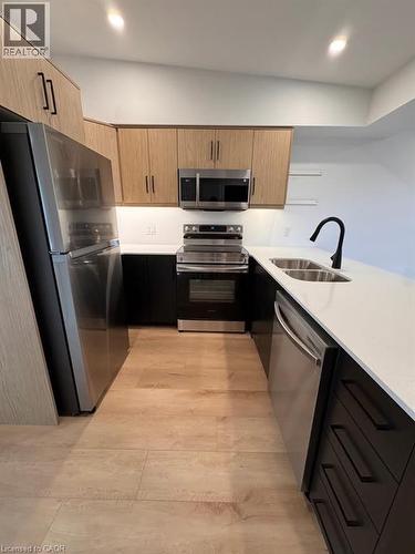 Modern kitchen featuring stainless steel appliances, light wood-finish upper cabinetry, dark lower cabinetry, and a white countertop with an undermount sink - 431 Krug Street, Kitchener, ON - Indoor Photo Showing Kitchen With Double Sink