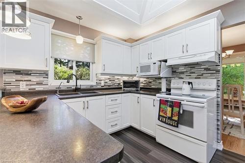 Contemporary kitchen featuring white cabinetry, dark countertops, a mosaic tile backsplash, wood-finish flooring, and a skylight - 26 Sideroad 18, Fergus, ON - Indoor Photo Showing Kitchen With Double Sink
