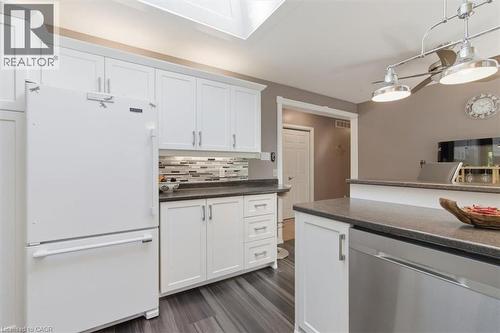 Kitchen featuring white cabinetry, dark countertops, a mosaic tile backsplash, wood-finish flooring, and a stainless steel dishwasher - 26 Sideroad 18, Fergus, ON - Indoor Photo Showing Kitchen
