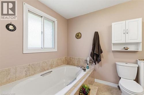 Soaking tub with a tiled surround, white sliding window, white wall-mounted storage cabinet with shelving, and tile flooring - 26 Sideroad 18, Fergus, ON - Indoor Photo Showing Bathroom