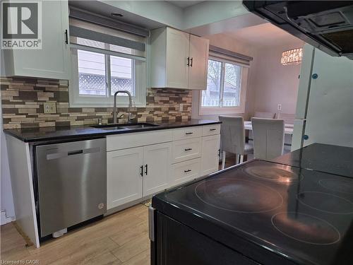 Kitchen featuring white cabinetry, dark countertops, a mosaic tile backsplash, a stainless steel dishwasher, and wood-finish flooring - 261 Overlea Drive, Kitchener, ON 