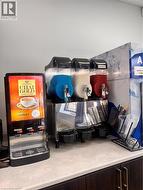 Beverage station featuring a chai dispenser, triple slushie machine, and dedicated cup storage, all set on a light-toned countertop with dark wood-finish cabinetry - 