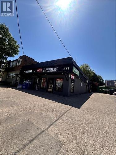 Commercial building with a dark facade, prominent signage, and a paved parking area - 277 Lancaster Street W, Kitchener, ON 