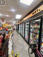Retail interior featuring a long aisle with commercial refrigerators, track lighting, ceiling panels, and tile flooring - 