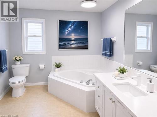 Bathroom featuring a built-in corner soaking tub, a white vanity with an integrated sink, a large wall-mounted mirror, and neutral-toned flooring - 732 Angler Way, Waterloo, ON - Indoor Photo Showing Bathroom