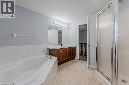 Bathroom featuring an integrated soaking tub with white tile surround, a separate shower enclosure with a frosted glass door, a wood-finish vanity with a light-colored countertop, and a large mirror w - 732 Angler Way, Waterloo, ON - Indoor Photo Showing Bathroom