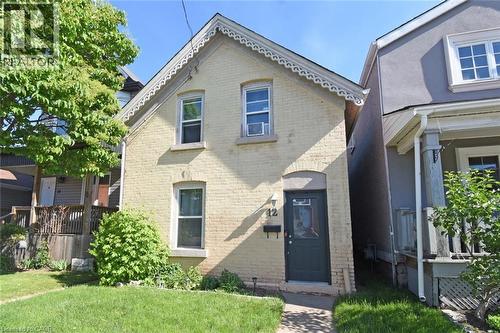 Brick exterior with decorative gable trim, a dark-colored entry door, and a manicured lawn - 12 Wood Street W, Hamilton, ON - Outdoor