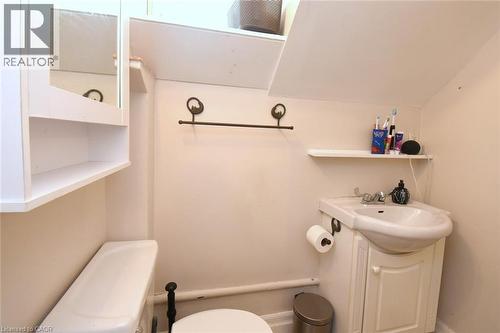Compact bathroom featuring a white porcelain toilet, pedestal sink with integrated vanity, mirrored medicine cabinet with open shelving, and wall-mounted towel bar - 12 Wood Street W, Hamilton, ON - Indoor Photo Showing Bathroom