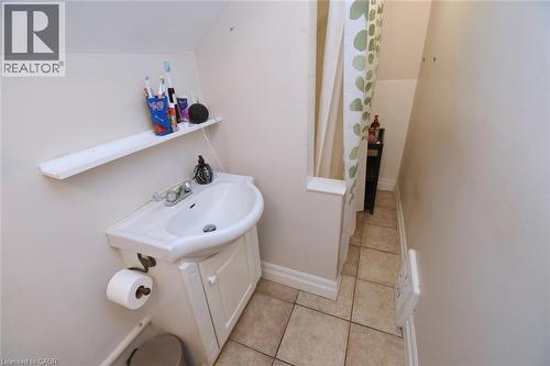 Compact bathroom featuring a white sink with a vanity cabinet, a wall-mounted shelf, and tiled flooring - 12 Wood Street W, Hamilton, ON - Indoor Photo Showing Bathroom