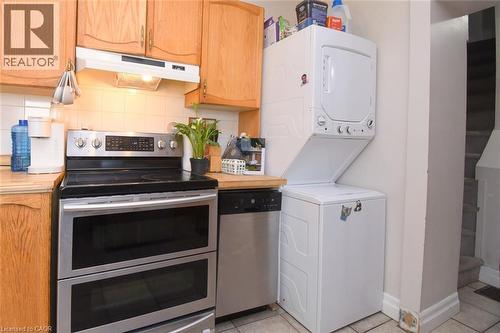 Kitchen space with light wood cabinetry, stainless steel double oven range, stainless steel dishwasher, and stacked white washer and dryer unit - 12 Wood Street W, Hamilton, ON - Indoor Photo Showing Kitchen