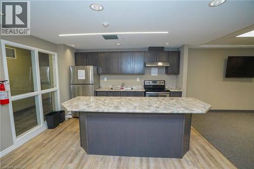 Kitchenette featuring gray wood-finish cabinetry, stainless steel appliances including a refrigerator and range, a stone-finish countertop, and a central island with a stone-finish surface - 7 Kay Crescent Unit# 107, Guelph, ON 