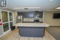 Kitchenette featuring gray wood-finish cabinetry, stainless steel appliances including a refrigerator and range, a stone-finish countertop, and a central island with a stone-finish surface - 