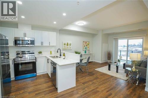 Open-concept living space with wood-finish flooring, white cabinetry, stainless steel appliances, and a sliding glass door leading to a balcony - 7 Kay Crescent Unit# 107, Guelph, ON 