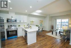 Open-concept living space with wood-finish flooring, white cabinetry, stainless steel appliances, and a sliding glass door leading to a balcony - 
