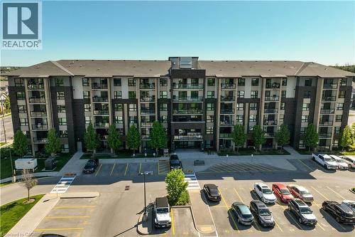Contemporary multi-story building featuring a dark brick and light-colored façade, multiple private balconies with glass railings, a pitched roof, and a prominent front entrance - 7 Kay Crescent Unit# 107, Guelph, ON 