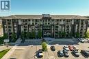 Contemporary multi-story building featuring a dark brick and light-colored façade, multiple private balconies with glass railings, a pitched roof, and a prominent front entrance - 7 Kay Crescent Unit# 107, Guelph, ON 