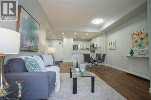 Open-concept living space with wood-finish flooring, recessed lighting, and a white kitchen featuring stainless steel appliances - 7 Kay Crescent Unit# 107, Guelph, ON 