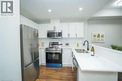 Modern kitchen featuring stainless steel appliances, white cabinetry, a double basin sink with a matte black faucet, light-toned countertops, and wood-finish flooring - 