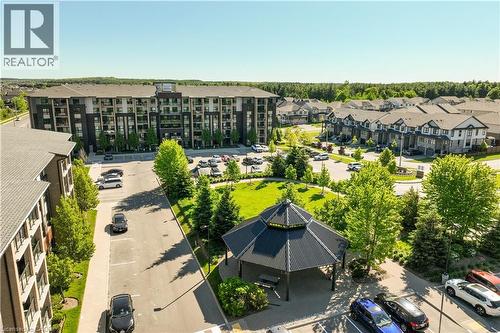 Modern multi-story residential building with balconies, surrounded by paved parking areas and green spaces - 7 Kay Crescent Unit# 107, Guelph, ON 