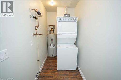 Dedicated utility area featuring a stacked washer and dryer, water heater, and wood-finish flooring - 7 Kay Crescent Unit# 107, Guelph, ON 