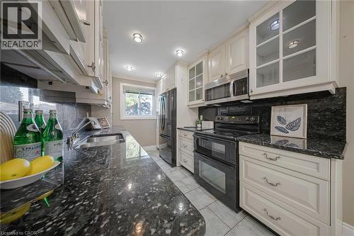 Galley kitchen featuring dark granite countertops, cream-painted cabinetry, and stainless steel appliances - 124 Dunsmere Drive, Kitchener, ON - Indoor Photo Showing Kitchen