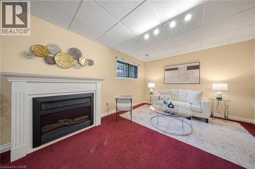 Fireplace featuring a white mantel, red carpeting, drop ceiling, track lighting, and a window with security bars - 124 Dunsmere Drive, Kitchener, ON - Indoor Photo Showing Living Room With Fireplace
