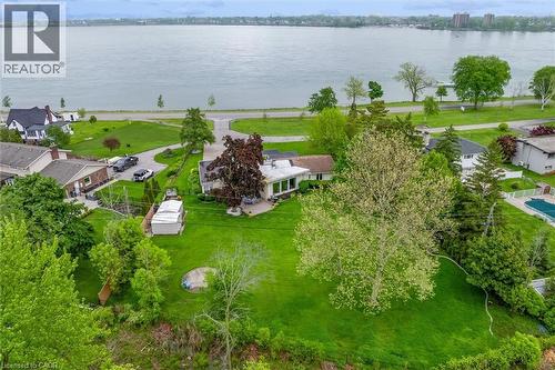 Expansive property featuring a waterfront setting, manicured green lawns, mature trees, a private circular driveway, and a spacious rear patio - 899 Niagara Parkway, Fort Erie, ON 