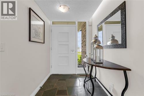 Entryway featuring natural slate tile flooring, a modern white door with frosted glass sidelight, stone exterior accents, and a flush-mount ceiling light fixture - 899 Niagara Parkway, Fort Erie, ON 