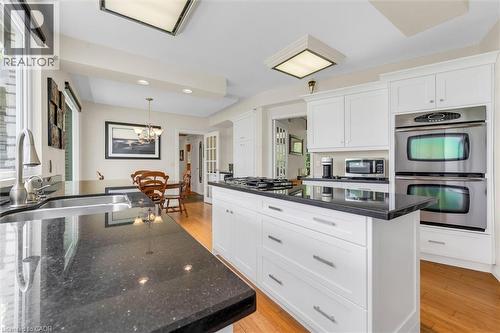Modern kitchen featuring white cabinetry, dark speckled countertops, stainless steel double wall ovens, a center island with a built-in cooktop, and wood-finish flooring - 899 Niagara Parkway, Fort Erie, ON 