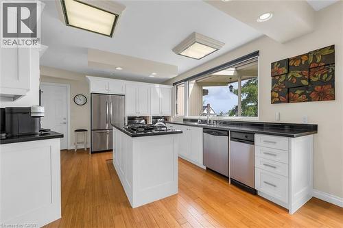 Kitchen featuring light wood-finish flooring, white cabinetry, dark countertops, a central island with a built-in cooktop, and stainless steel appliances - 899 Niagara Parkway, Fort Erie, ON 