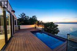 Expansive exterior deck with a built-in swimming pool, composite decking, glass railing, and water feature - 