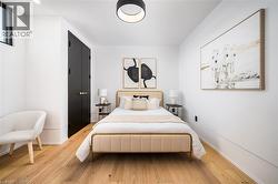 Chic room featuring light wood-finish flooring, white walls, a black double-door closet with brass hardware, and a modern ceiling light fixture - 