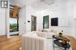 Bright interior space featuring wood-finish flooring, a modern open-tread staircase, a glass-enclosed elevator, recessed lighting, and a contemporary ceiling fixture - 