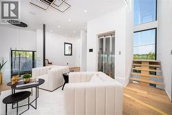 Open concept living area featuring light wood-finish flooring, a contemporary staircase with glass paneling, a built-in elevator, and abundant natural light from large windows - 