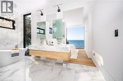 Contemporary bathroom featuring a freestanding soaking tub, dual vanity with undermount sinks, and a full-height window overlooking a body of water - 