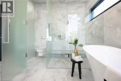 Bathroom featuring a freestanding white soaking tub, large format marble-look wall and floor tiling, a walk-in shower with a built-in bench, and a privacy glass enclosure for the commode - 6 Firelane 11A Street, Niagara-On-The-Lake, ON - Indoor Photo Showing Bathroom
