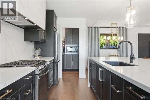 Contemporary kitchen featuring dark cabinetry, light countertops, wood-finish flooring, a kitchen island with an integrated sink and black faucet, and a large window with exterior greenery - 71 Miles Road, Hamilton, ON 