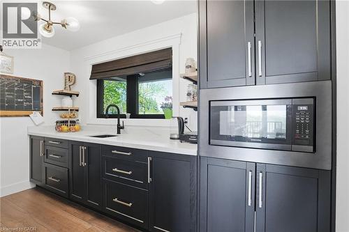 Built-in microwave oven surrounded by dark cabinetry with polished hardware, white countertops, and a black sink with a matching faucet - 71 Miles Road, Hamilton, ON 