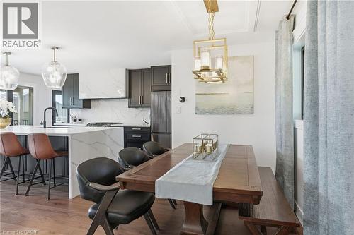 Open-concept kitchen and dining area featuring dark cabinetry, white countertops, a built-in range hood with matching backsplash, and wood-finish flooring - 71 Miles Road, Hamilton, ON 